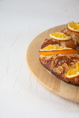 Detail of homemade Rosc&oacute;n de Reyes with orange and almonds, on a wooden plate, vertical, white background, typical Spanish Christmas dessert, with copy space