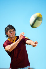 Sport, ball and male rugby player catching in training on a blue sky background. Professional athlete, uniform and confident fit exercise or workout for fitness game with a sportsman outdoors