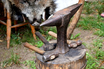 A close up on a set of equipment, tools, and ingredients used by a blacksmith, woodworker, archer, or cloth maker seen on a table located next to a tent on a sunny summer day