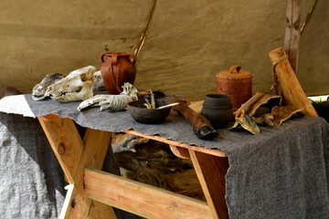 A close up on a set of equipment, tools, and ingredients used by a blacksmith, woodworker, archer, or cloth maker seen on a table located next to a tent on a sunny summer day