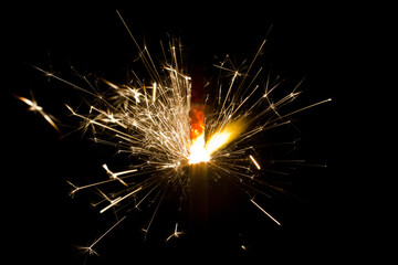Glowing Sparkler Emanating Golden Sparks Against Dark Background