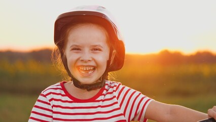 Girl with lost tooth stands with laughter in field. Girl wearing helmet stands laughing echoing...