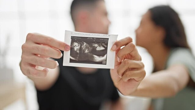 Beautiful couple holding ultrasound baby sitting on bed kissing at bedroom
