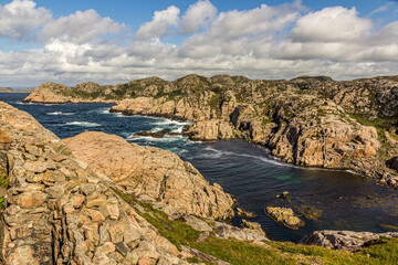 Fototapeta na wymiar Rocky coast of Norway, mountains covered with moss and grass strong currents and dangerous cliffs. Cumulus clouds against a bright blue sky. Near Lindesnes Lighthouse, North Sea.