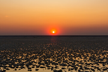 Sunset or sunrise on salt lake Elton (Russia) with mirror or reflection of low Cumulostratus or Stratocumulus clouds in the brine at golden hour with the sun in the background. Evening or morning.