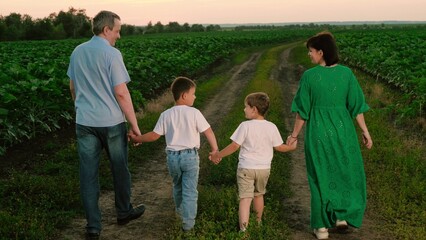 Mom dad and kids walk holding hands through vegetable garden together. Children join hands with...