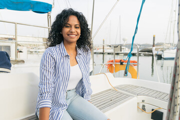 Glad ethnic female sitting on yacht deck
