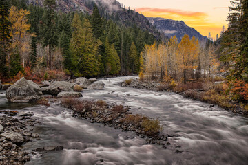 smooth winding stream in forest of northwestern United States with autumn foliage and coniferous trees in Washington state North Cascade Mountains and sunrise or sunset in background
