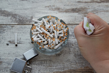 An overflowing ashtray with cigarette butts, a hand clutching an empty cigarette pack, close-up