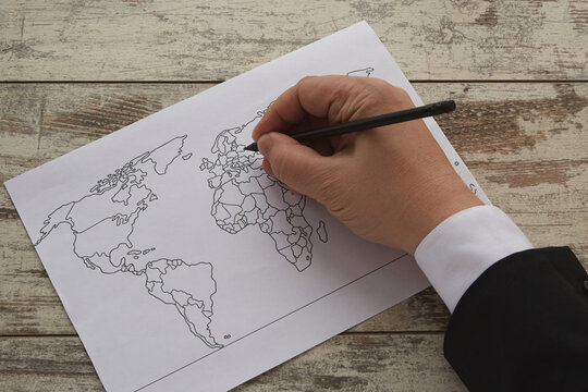 A hand draws a world map with a pencil on a white piece of paper. New world order, world news, new state borders, Eastern European problems