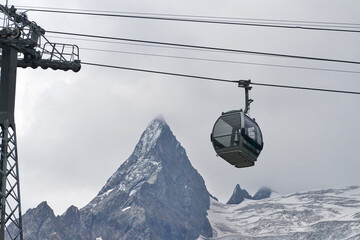 Cable car with gondola elevator against rocky snowy mountain in fog. Copy space.