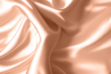 Abstract background, folds of silk fabric in peach fuzz color.