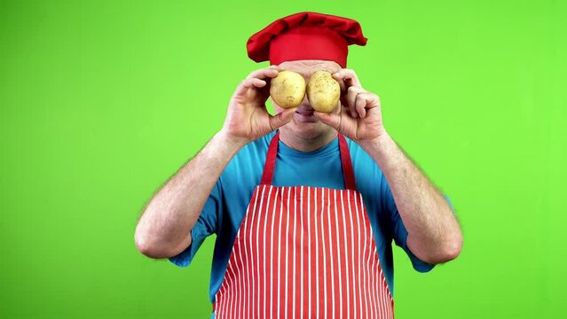 Cheerful senior chef covering eyes with potatoes.