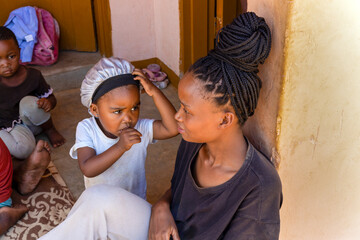 village african mother with braids and her kids in front of the house playing, little girl...