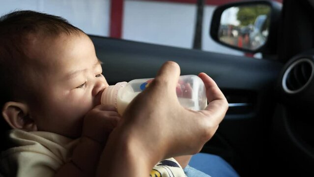 Baby girl drinking formula milk in bottle, mother feed her infant