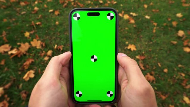 first person view of a guy walking and using both hands a smartphone with a green screen with trackers