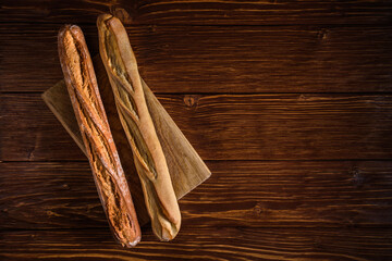 two baguettes lie side by side parallel on a cutting board on a textured plank wooden background....