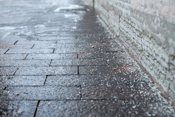 Deicing chemicals on pavement in winter. Salt grains on icy sidewalk, paving slab with rock salt in...
