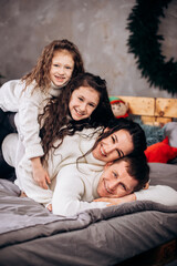Funny young parents mom dad with two daughters in white sweaters on the bed. Family day parenthood childhood concept