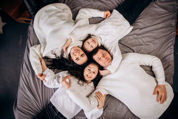 Funny young parents mom dad with two daughters in white sweaters on the bed. Family day parenthood childhood concept. Top view