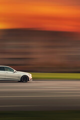 Fototapeta na wymiar A fast moving car. Car with abstract speed blur background in evening with orange sky. Side view of the front of the car