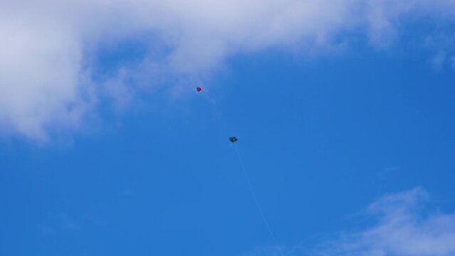 Two kites fighting aggressively with each other, kites gliding, swinging and fast movements in the blue sky with clouds