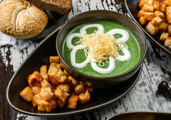Vegan spinach soup with cheese, sour cream and croutons in bowl on rustic wooden background. Healthy food, top view