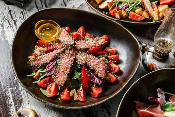 Healthy beef salad with sesame, arugula, tomatoes, lettuce in plate on rustic wooden background. Healthy food, top view