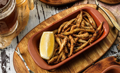 Tasty fried anchovies in cornmeal with lemon piece in wooden background, grilled small fish for...