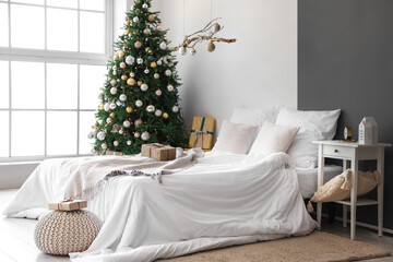 Interior of festive bedroom with comfortable bed, hanging decor and Christmas tree