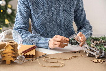 Woman decorating Christmas ball with rhinestones on table