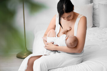 Happy mother breastfeeding her little cute baby in bedroom - obrazy, fototapety, plakaty