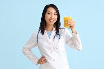 Female Asian nutritionist with glass of juice on blue background