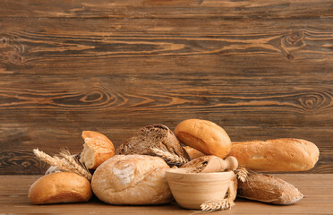 Loaves of different fresh bread with wheat spikelets and grains on wooden background