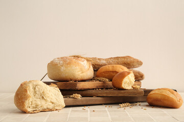 Boards with loaves of different fresh bread and wheat spikelets on white tiled table