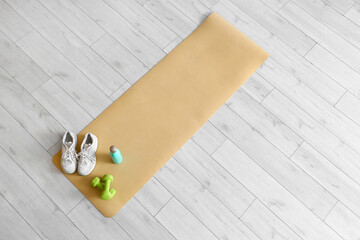 Fitness mat with sneakers, dumbbells and water bottle on floor, top view
