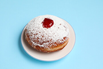 Tasty donut with jam for Hanukkah celebration on blue background, closeup