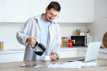 Young man pouring coffee and newspapers on table in kitchen - obrazy, fototapety, plakaty