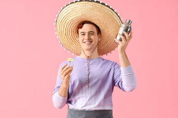 Young male bartender in sombrero hat with shot of tequila and shaker on pink background