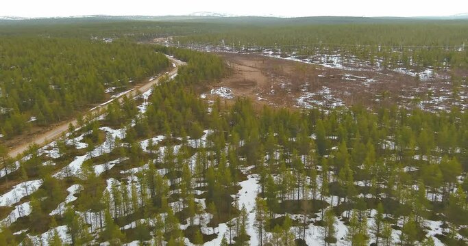 Aerial landscape view of forest, swamp and gravel road in cloudy spring weather with snow on the ground, Sodankylä, Lapland, Finland.