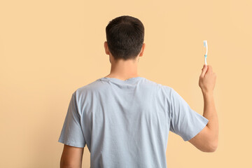 Handsome man with toothbrush on beige background, back view