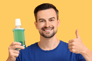 Handsome man with mouth rinse showing thumb-up on yellow background, closeup