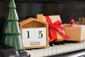 Calendar with text 15 DAYS UNTIL HOLIDAYS, Christmas gifts and decor on piano keys, closeup