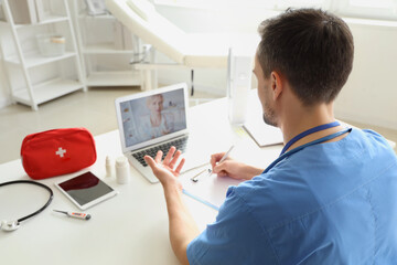 Fototapeta na wymiar Young doctor video chatting with patient on laptop in office