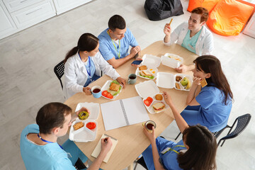 Team of doctors having lunch at table in hospital kitchen, top view