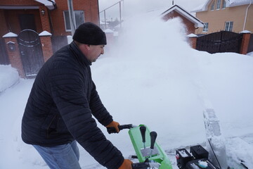 A man cleans snow in the winter in the courtyard of the house,  man cleaning snow with a snow blower