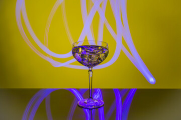 Close-up view of glass of alcohol with ice against yellow-blue abstract backdrop.