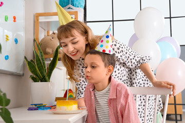 Mother and her cute little boy blowing out candle on birthday cake in decorated room
