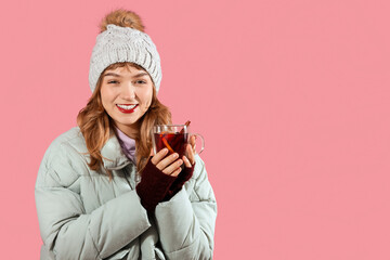 Smiling young woman in winter clothes with mulled wine on pink background