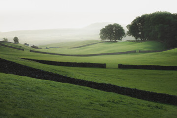 Moody atmospheric mist along old stone walls and rolling hills in the rural English countryside of Wensleydale, Yorkshire Dales National Park.